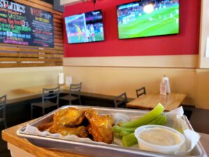 Plate of wings in foreground. Two televisions with images of soccer in background.