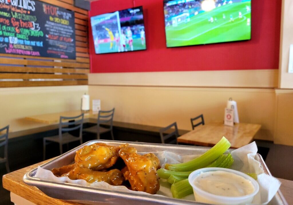 Plate of wings in foreground. Two televisions with images of soccer in background.